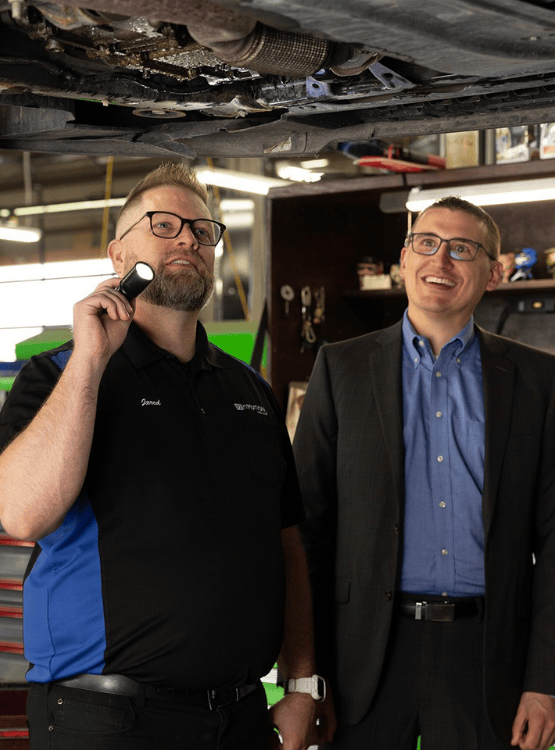 Mechanic and banker inspecting the underside of a vehicle in shop. 