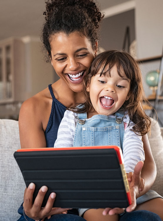 Smiling young mother with her daughter on her lap playing a game on a tablet. 