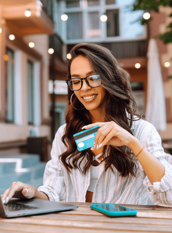 Woman with long hair wearing glasses holding a debit card shopping online.