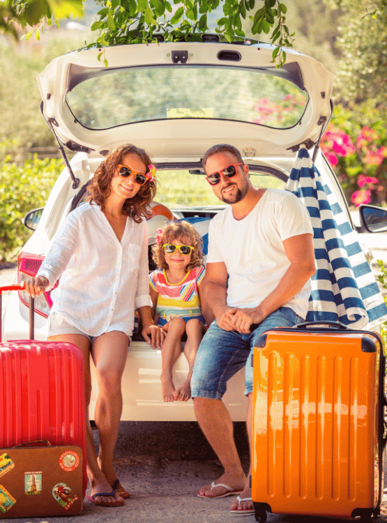 A family sitting on the back of their car in summer with their colorful suitcases going on vacation.