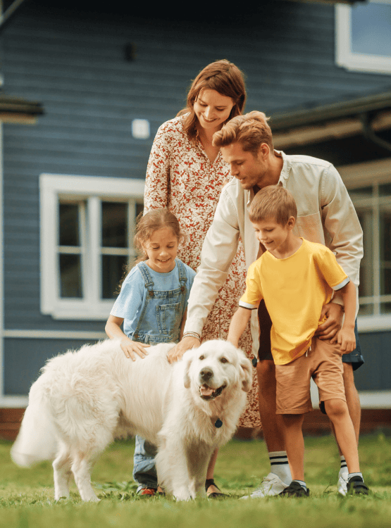 A young family of 4 playing with their dog in the backyard of their home.