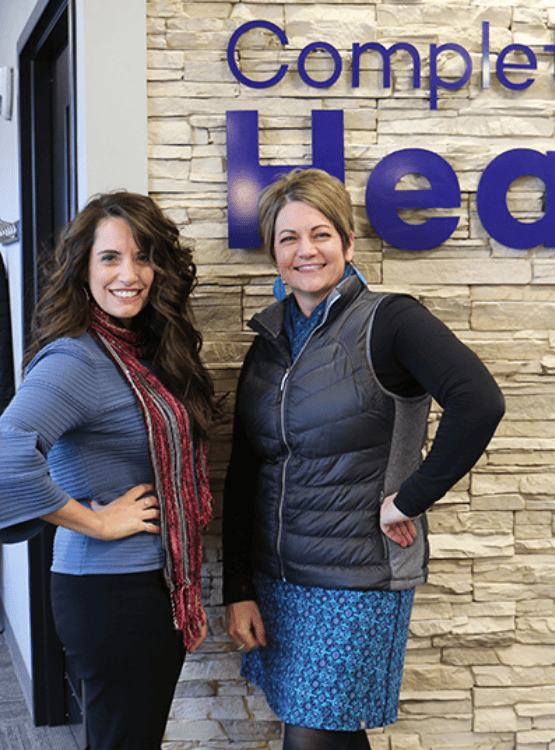 Two women owners of Complete Hearing standing in front of a limestone wall.