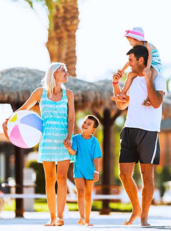 A young family walking near the beach with a beachball. 